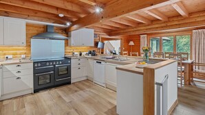 Une cuisine rustique aménagée dans une cabane en bois, avec un îlot central, un four encastré et une grande fenêtre donnant sur la verdure.