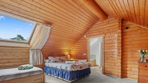 Une chambre confortable dans un chalet en rondins, avec un lit, un banc et une petite table sur laquelle est posé un vase.