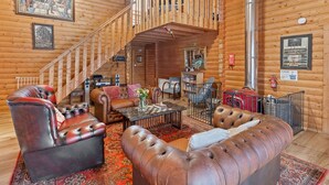 L’intérieur d’une cabane en rondins, avec un escalier, des canapés en cuir, une table basse et des œuvres d’art accrochées aux murs.