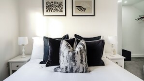 Una cama bien hecha con almohadillas estampadas en blanco y negro, ropa de cama blanca y dos cuadros en la pared.