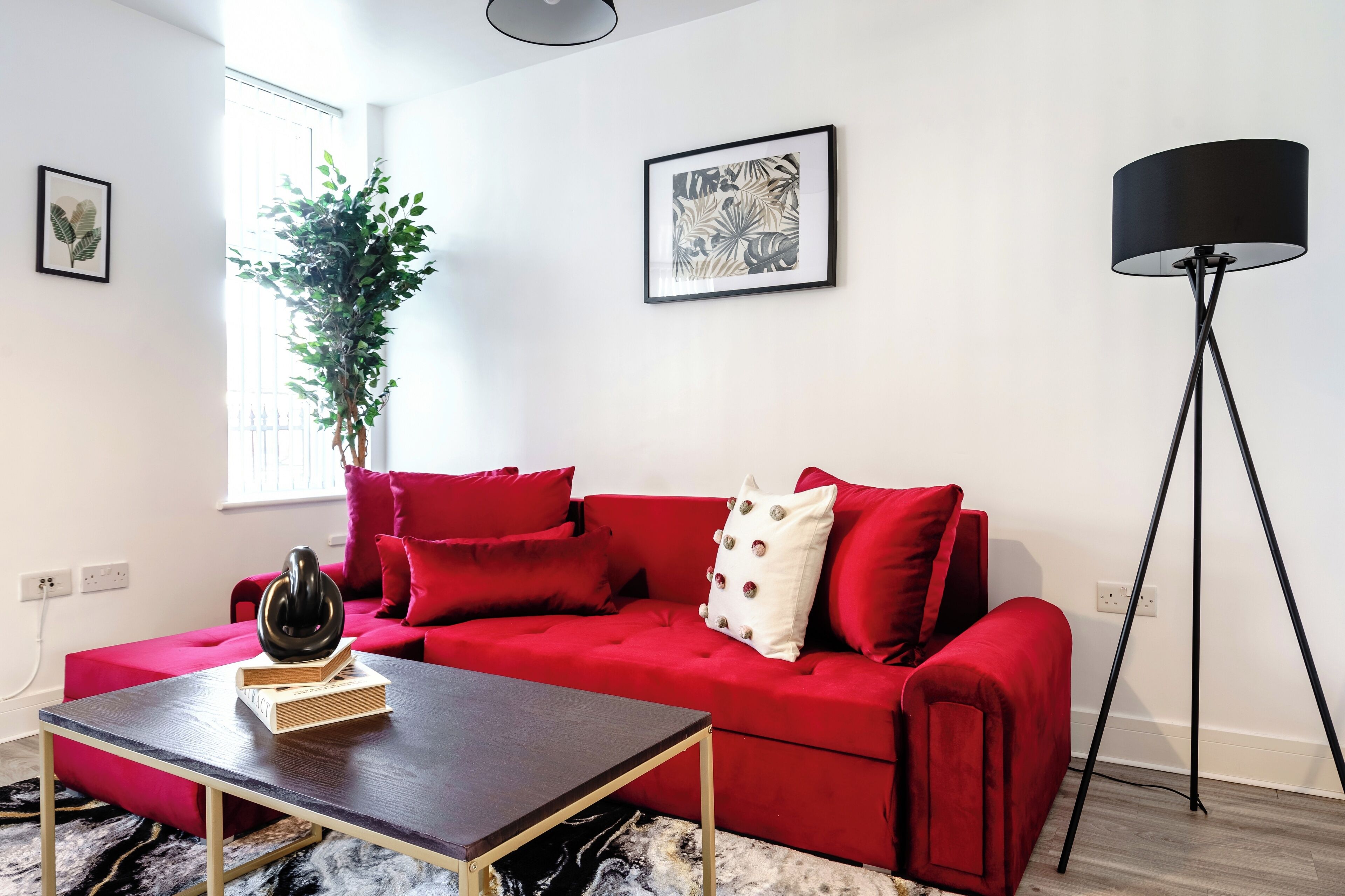 A modern living room with a red sofa, a wooden coffee table, a floor lamp, and a large plant.