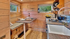 A compact kitchen with wooden walls, a dining area with a bench, and a window providing a view of the outdoors. - Beautiful  villa for 2 guests (Dingwall)