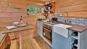 A kitchen with wooden walls, a window, a sink, and a countertop with various items. - Beautiful  villa for 2 guests (Dingwall)