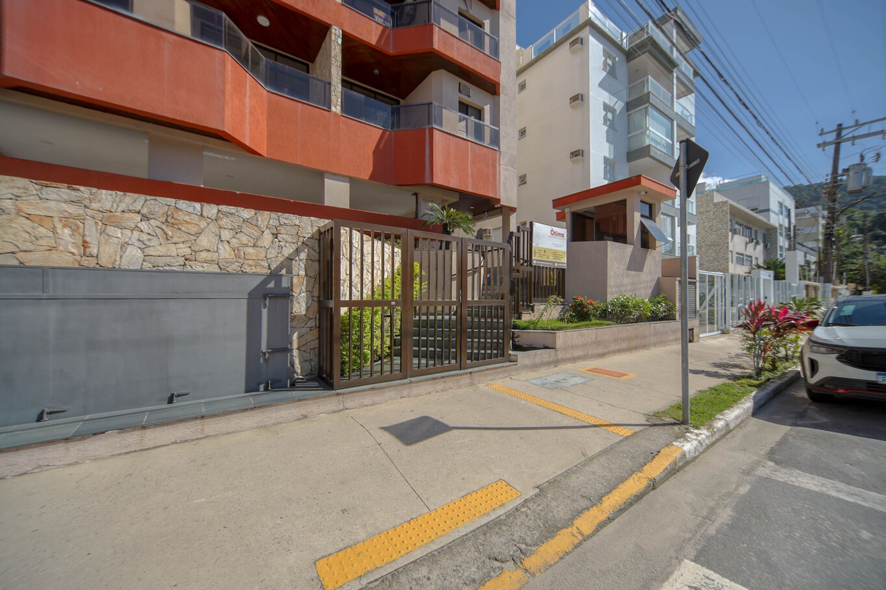 Un moderno edificio de apartamentos con fachada de piedra, entrada protegida por una reja y un coche blanco estacionado en la calle.