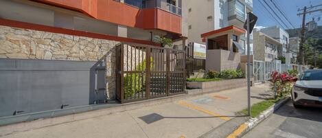 Un moderno edificio de apartamentos con fachada de piedra, entrada protegida por una reja y un coche blanco estacionado en la calle.