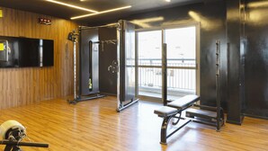 Une salle de sport avec un plancher en bois, du matériel d’exercice, un banc et une grande fenêtre.