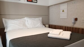 Une chambre d’hôtel équipée d’un lit, d’une table de chevet, d’un téléphone fixé au mur et d’un panneau d’affichage des consignes de sécurité.