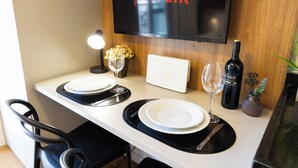 Un coin repas avec une table dressée pour deux personnes, un téléviseur fixé au mur affichant le logo de Netflix, une bouteille de vin et une petite plante en pot.