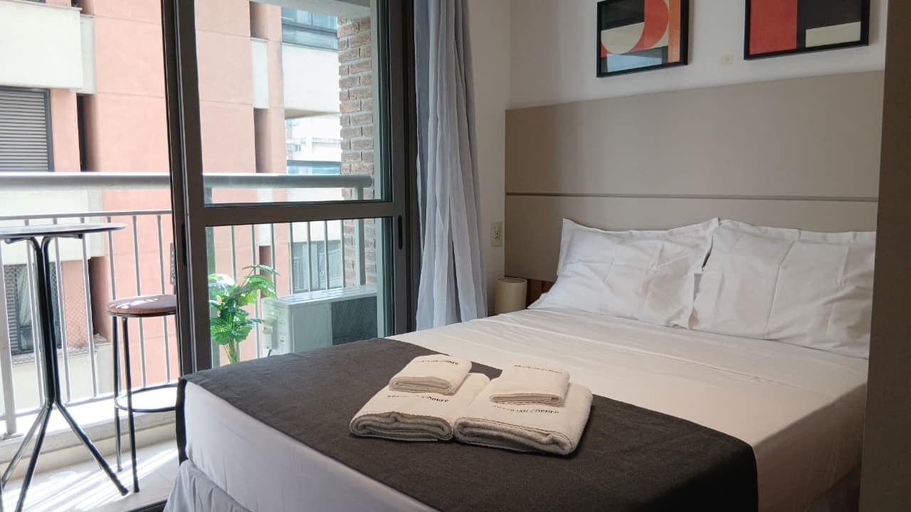 A hotel room with a bed, a window, a balcony, and a plant.