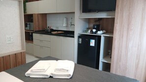 A compact kitchen with a refrigerator, a microwave, and a coffee maker. There is a table with folded towels and a television mounted on the wall. - Pool & AC Steps from Ibirapuera (Sao Paulo)
