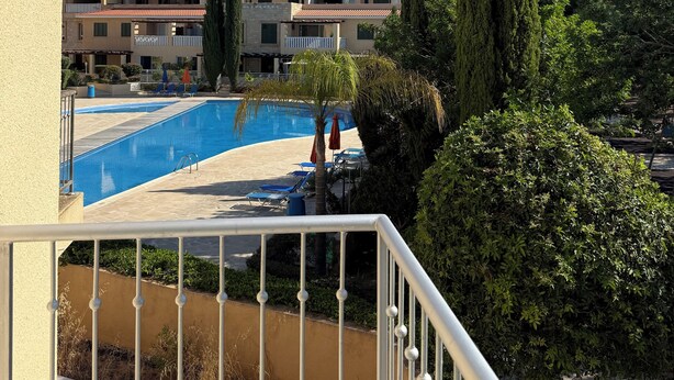 A pool area with a clear blue sky, a well-maintained pool, and a view of multi-story buildings in the background.