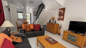 A modern living room with a black sofa, wooden coffee table, and a TV on a wooden cabinet. A staircase is visible in the background.