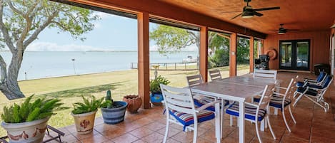 Un patio exterior con mesa y sillas, plantas en macetas y vista al agua.