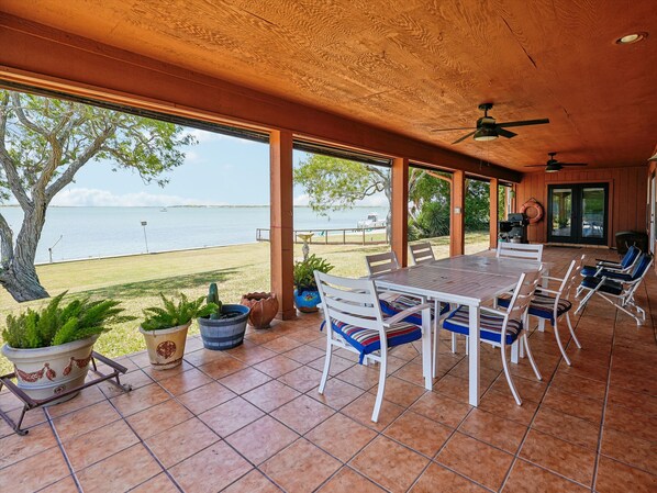 Une terrasse extérieure avec une table et des chaises, des plantes en pot et une vue sur l’eau.