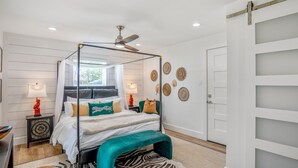 A modern bedroom with a four-poster bed, a ceiling fan, and a zebra-patterned rug. - Sandy Toes Retreat | Charming, Pool Access (Galveston)
