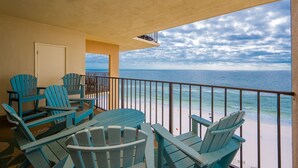 A balcony with blue Adirondack chairs and a table, overlooking a beach with a railing. - Phoenix I 1141 3 Bedroom Condo (Orange Beach)