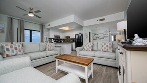 A modern living room with a sofa set, a wooden coffee table, and a kitchen in the background. - Phoenix I 1141 3 Bedroom Condo (Orange Beach)