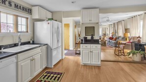A spacious kitchen with white cabinets, a refrigerator, and a sink. There is a dining area with a sofa and a coffee table. - Home Port - Spacious Retreat In Prime Location 4 Bedroom Home (Davis)