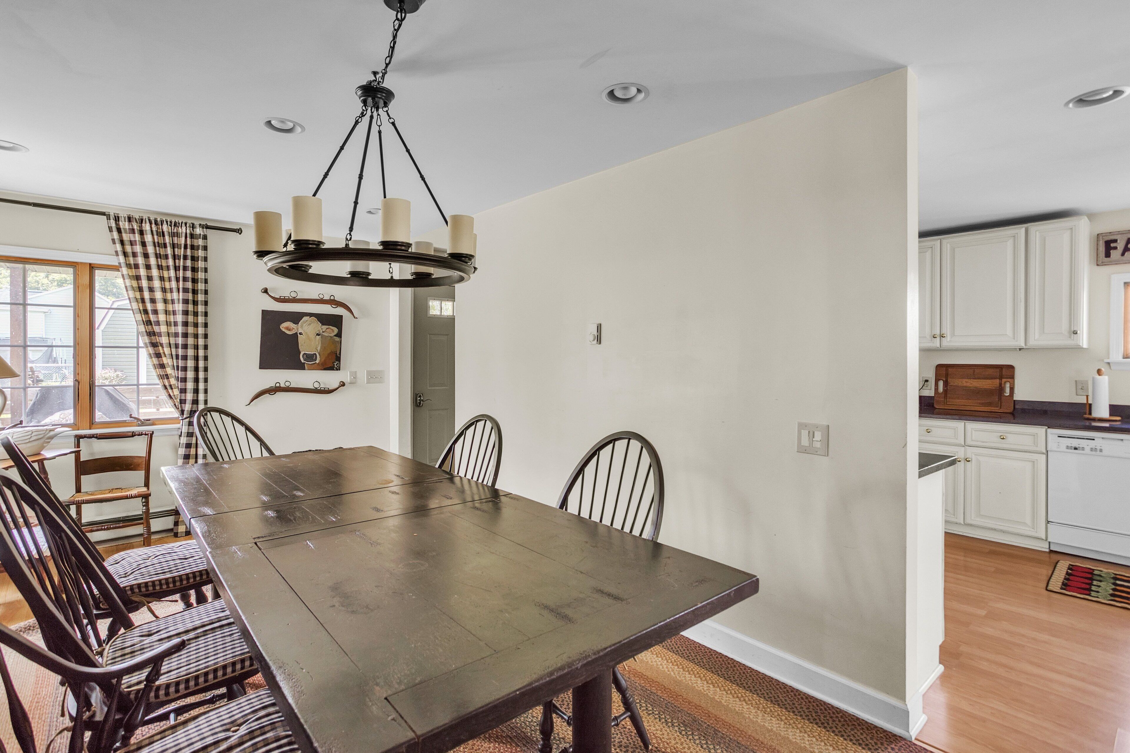 A dining room with a large wooden table and chairs, a chandelier, and a view of the kitchen.