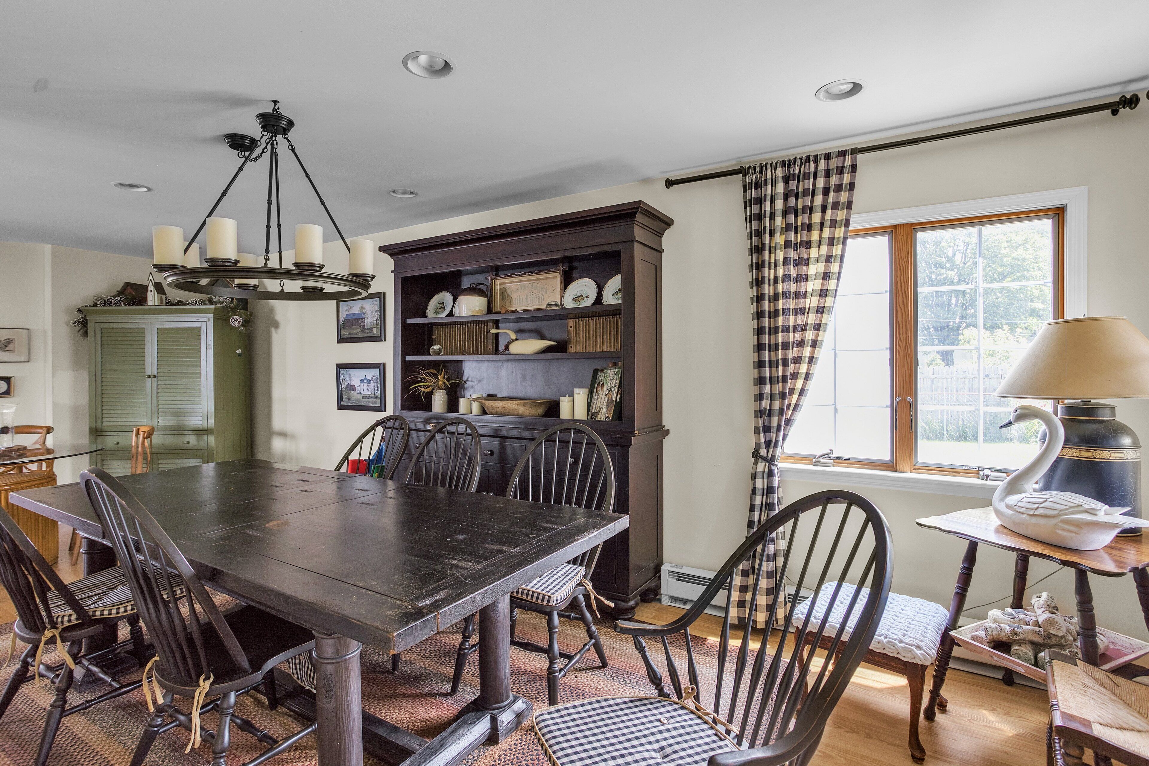 A dining area with a dark wooden table and chairs, a chandelier, and a bookshelf with decorative items.