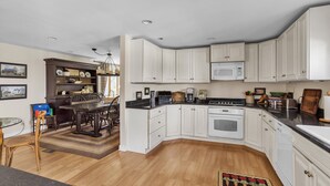 A modern kitchen with white cabinets, a microwave, a stove, and a dining area with a table and chairs. - Home Port - Spacious Retreat In Prime Location 4 Bedroom Home (Davis)