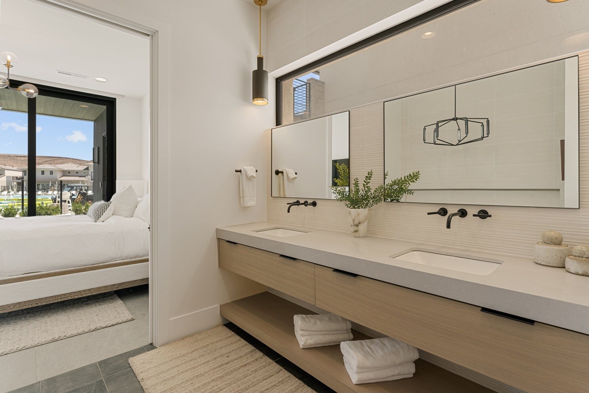 A modern bathroom with a large mirror, dual sinks, and a bed with a view of the outside.
