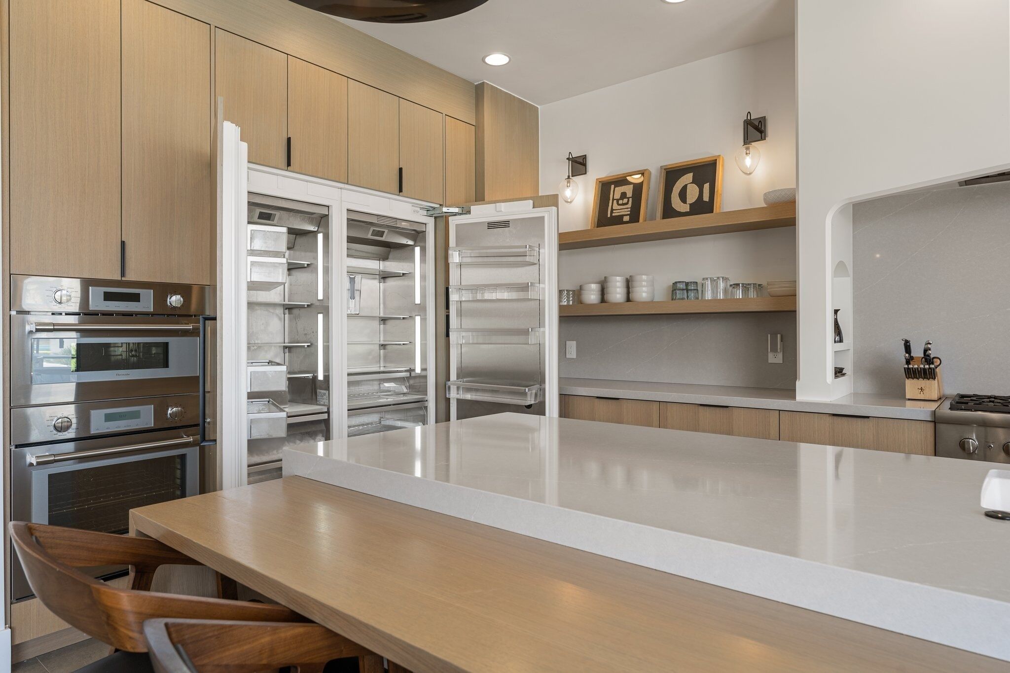 A modern kitchen with built-in ovens, a large island, and wooden cabinets.
