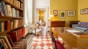 Ein gemütliches Zimmer mit einem Holzbücherregal voller Bücher, einem Schachbrettfußboden, einem Holztisch, einem Stuhl und einem Bett mit gemusterten Bettbezügen.