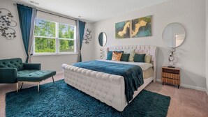 Un dormitorio con una cama grande, una silla, una mesita de noche y una obra de arte en la pared.