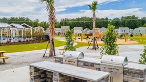 Un patio al aire libre con una estación de barbacoa de piedra, una mesa de picnic y palmeras.