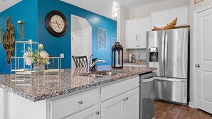 Una cocina moderna con armarios blancos, una pared azul de acento, electrodomésticos de acero inoxidable y una encimera de granito.