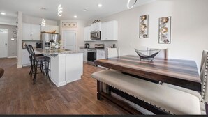 Una cocina moderna con armarios blancos, electrodomésticos de acero inoxidable y una mesa de comedor de madera con un banco.