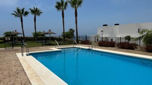 A swimming pool with a wooden deck, palm trees, and a white building in the background. - Holiday Home 'Great Townhouse Close To The Beach' with Sea View, Wi-Fi and Air Conditioning (Manilva)