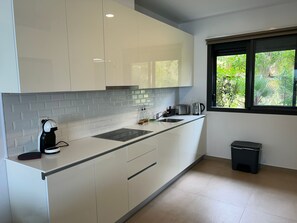 Eine moderne Küche mit weißen Schränken, einer schwarzen Arbeitsplatte, einer Kaffeemaschine, einem Toaster und einem Fenster mit Blick auf Grünflächen.