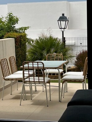 Une terrasse extérieure avec une table et des chaises, un lampadaire et un mur blanc en arrière-plan.