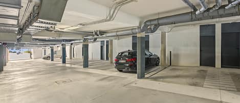 A parking garage with concrete floors, metal pillars, and overhead pipes.