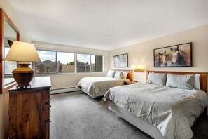 Une chambre avec deux lits, une commode en bois, une lampe et un tableau représentant des chevaux.