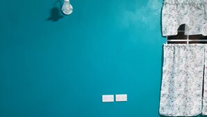 Una habitación con paredes color turquesa, un sofá gris, dos tomas de corriente, una lámpara y cortinas con estampado floral.