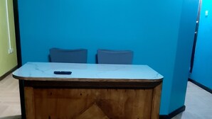 Un escritorio de madera con cubierta de mármol, dos sillas y un mueble bajo en una habitación con paredes azules y suelo de baldosas.