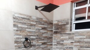 Ducha con pared de diseño tipo piedra, un aro para toalla negro y una ventana blanca sobre la ducha.