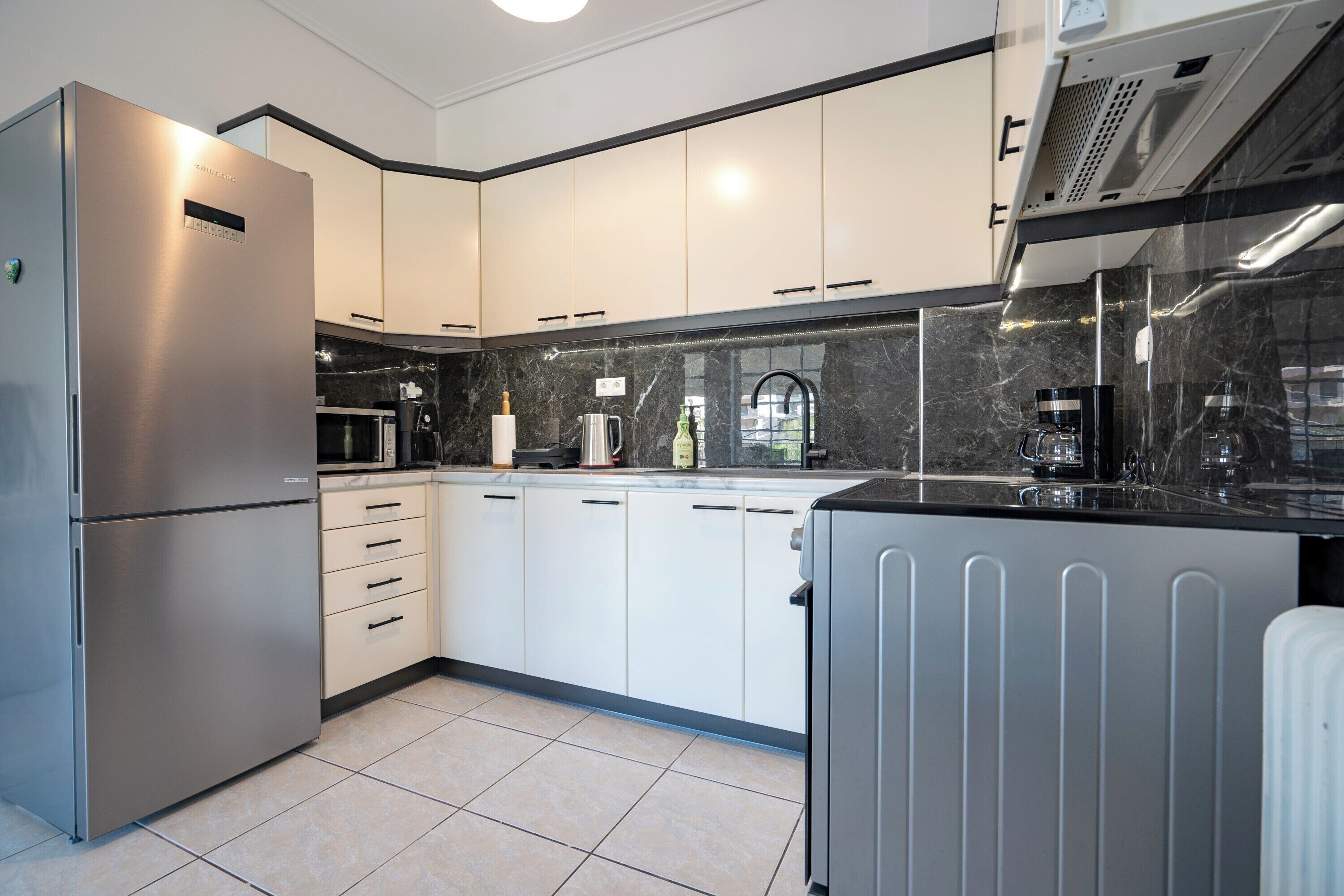 A modern kitchen with white cabinets, a stainless steel refrigerator, a black countertop, and a built-in oven.