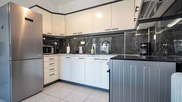 A modern kitchen with white cabinets, a stainless steel refrigerator, a black countertop, and a built-in oven.