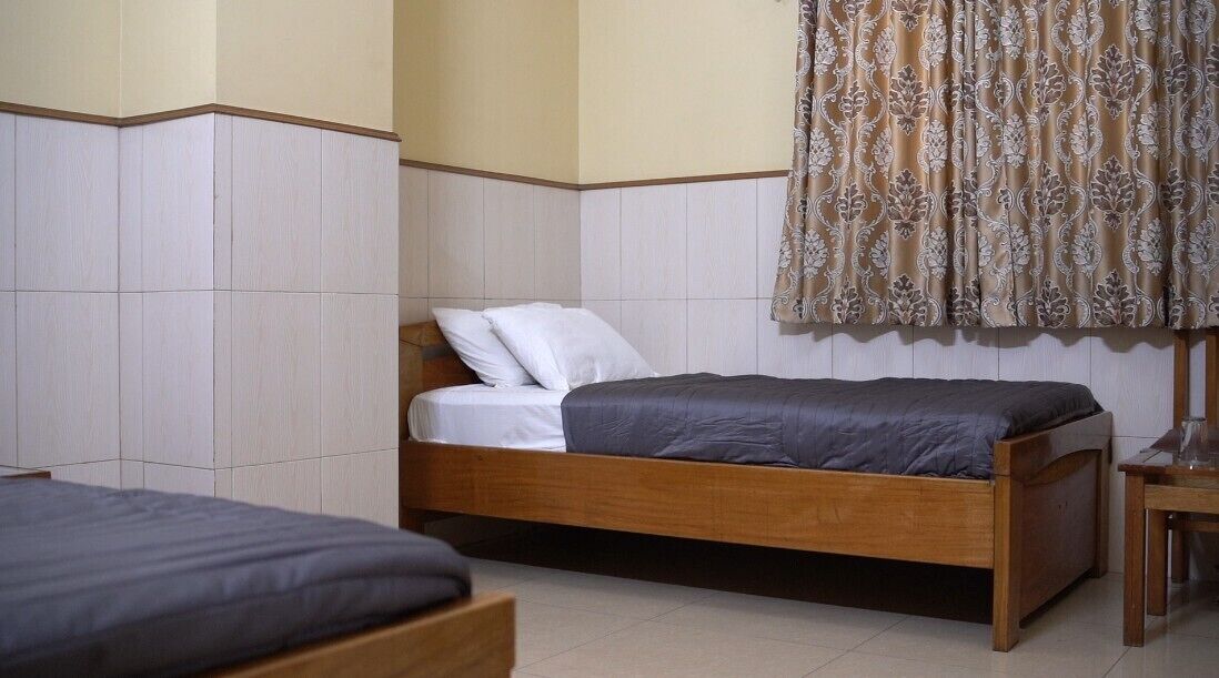 A bedroom with two beds, a wooden headboard, a bedside table, and a patterned curtain.