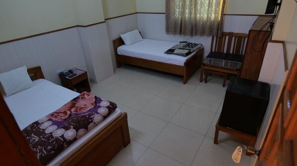 Habitación de hotel con dos camas individuales, un escritorio pequeño, una silla, un televisor y una ventana con cortinas.