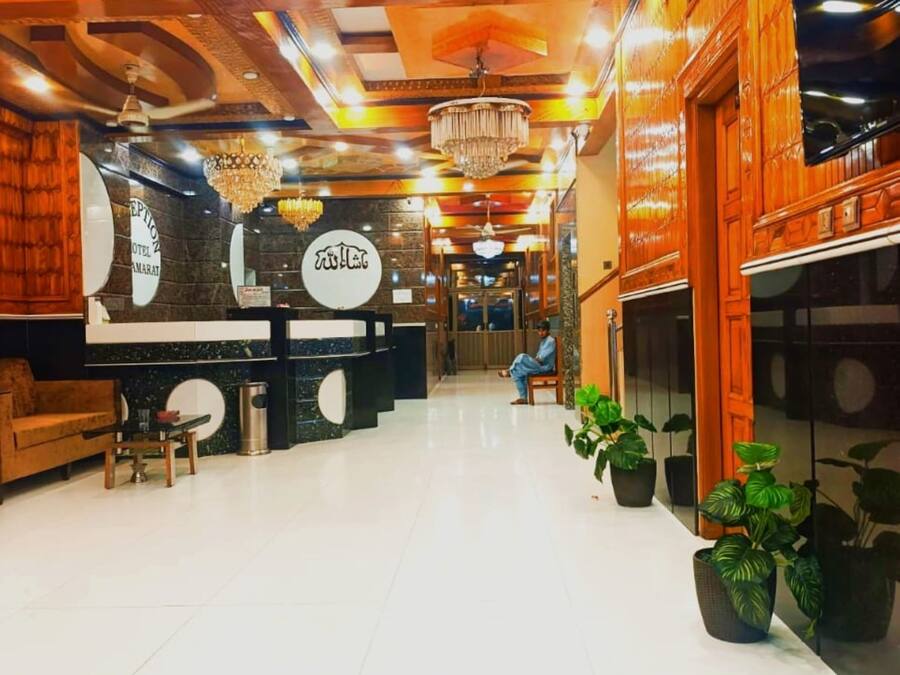 Um saguão de hotel com balcão de recepção, um candelabro e plantas em vasos.