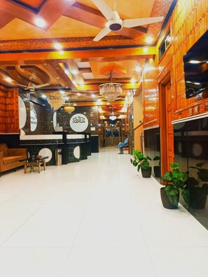 Un hall de hotel con mostrador de recepción, una araña de cristal y plantas en macetas.