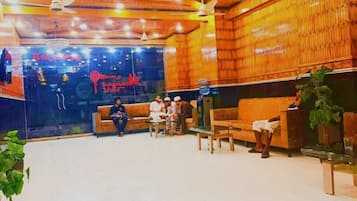 A spacious lobby with a high ceiling, wooden paneling, and a chandelier. There are several seating areas with sofas and chairs.
