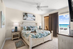 Quarto com cama, mesas de cabeceira, ventoinha no teto, um quadro e vista para o mar.