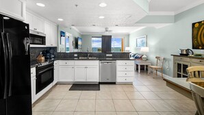 Una cocina moderna con armarios blancos, un refrigerador negro, un microondas, un lavavajillas y un comedor con mesa y sillas.