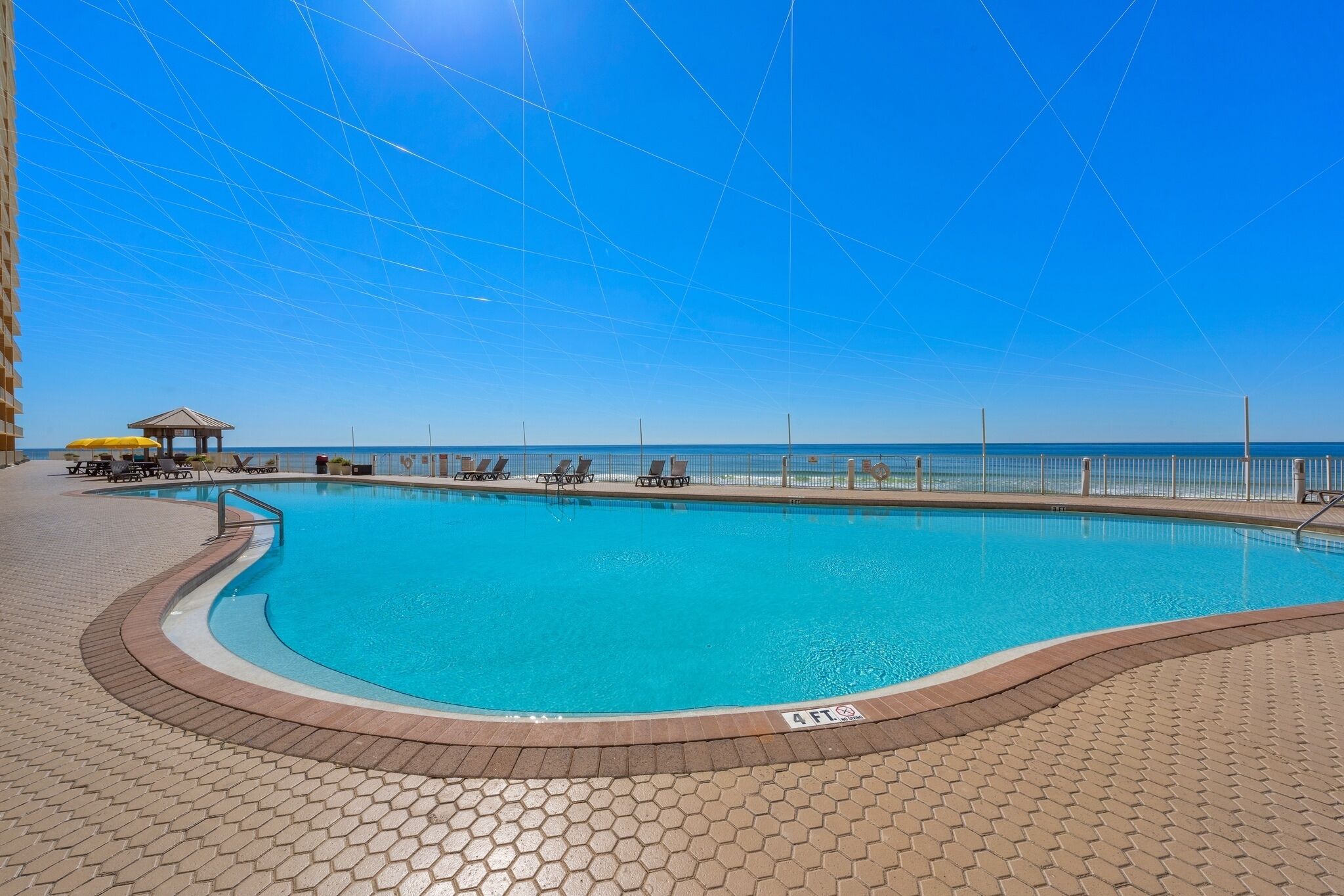 Une piscine dotée d’un parasol, de chaises longues et offrant une vue sur la mer.